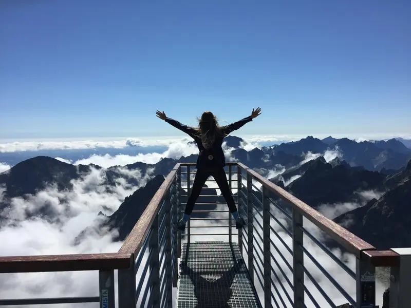 A person posing with their hands up in front of a mountainous landscape